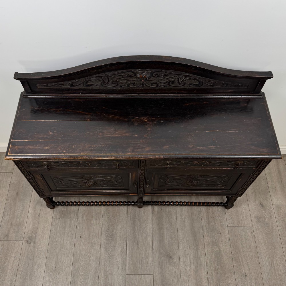 A dark oak 19th-century sideboard featuring carved lion mask motifs, scrollwork panel doors, and bobbin-turned legs connected by stretchers. View X