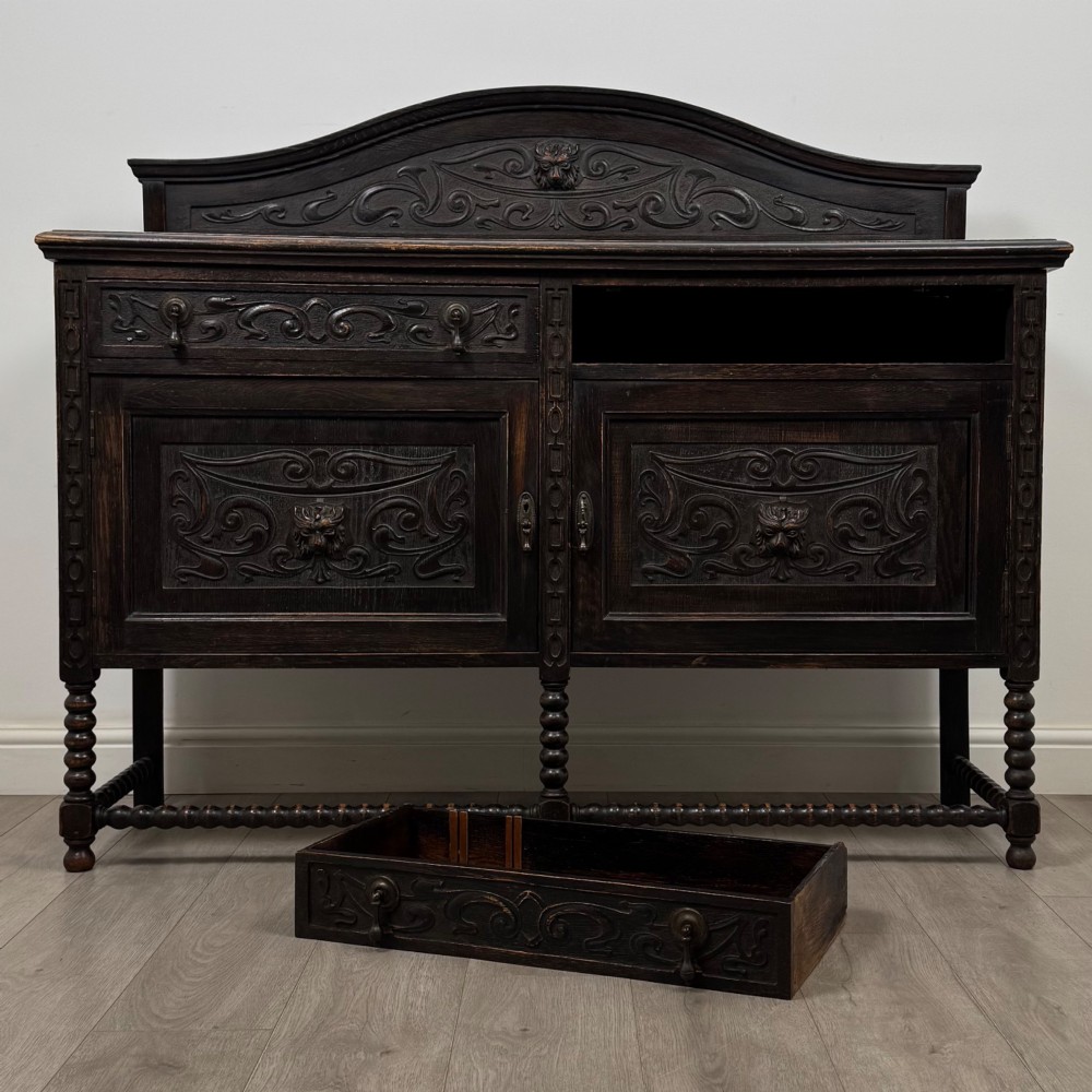 A dark oak 19th-century sideboard featuring carved lion mask motifs, scrollwork panel doors, and bobbin-turned legs connected by stretchers. View XI