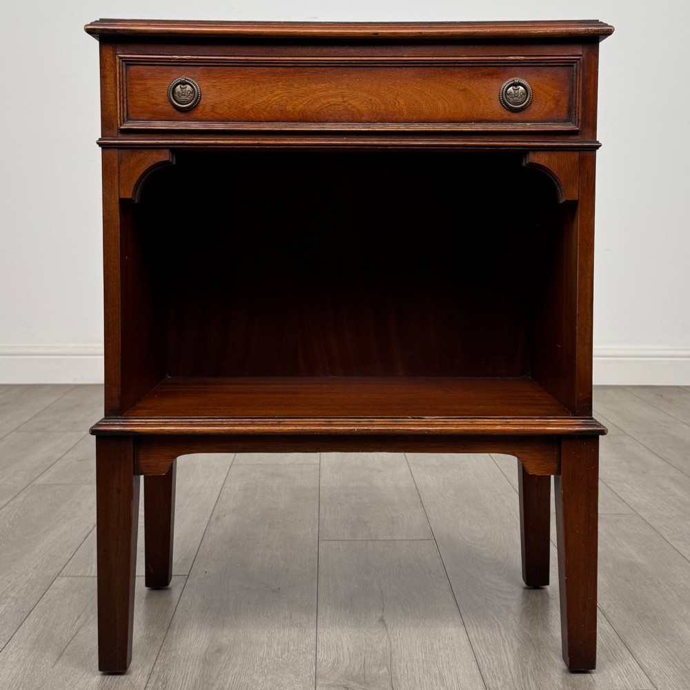 A small mahogany bedside cabinet with a top drawer, brass ring pull handles, an open lower shelf, and straight tapered legs.