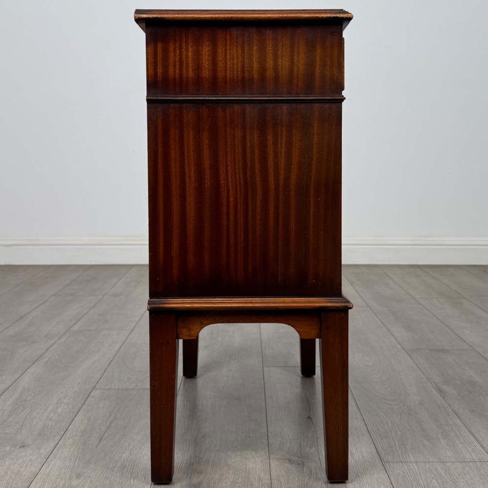 A small mahogany bedside cabinet with a top drawer, brass ring pull handles, an open lower shelf, and straight tapered legs. View VII