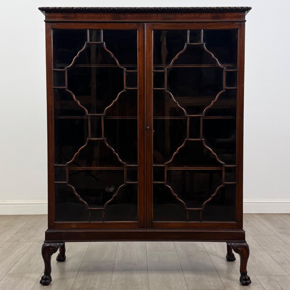 An Edwardian dark mahogany display cabinet featuring double astragal glazed doors and cabriole legs with carved claw and ball feet.