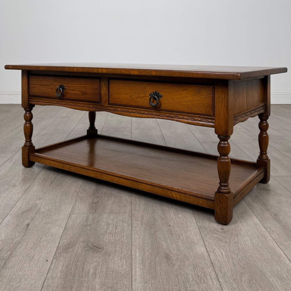 A rectangular warm brown oak coffee table featuring two drawers with metal ring handles, carved apron detailing, turned legs, and a lower storage shelf. View II