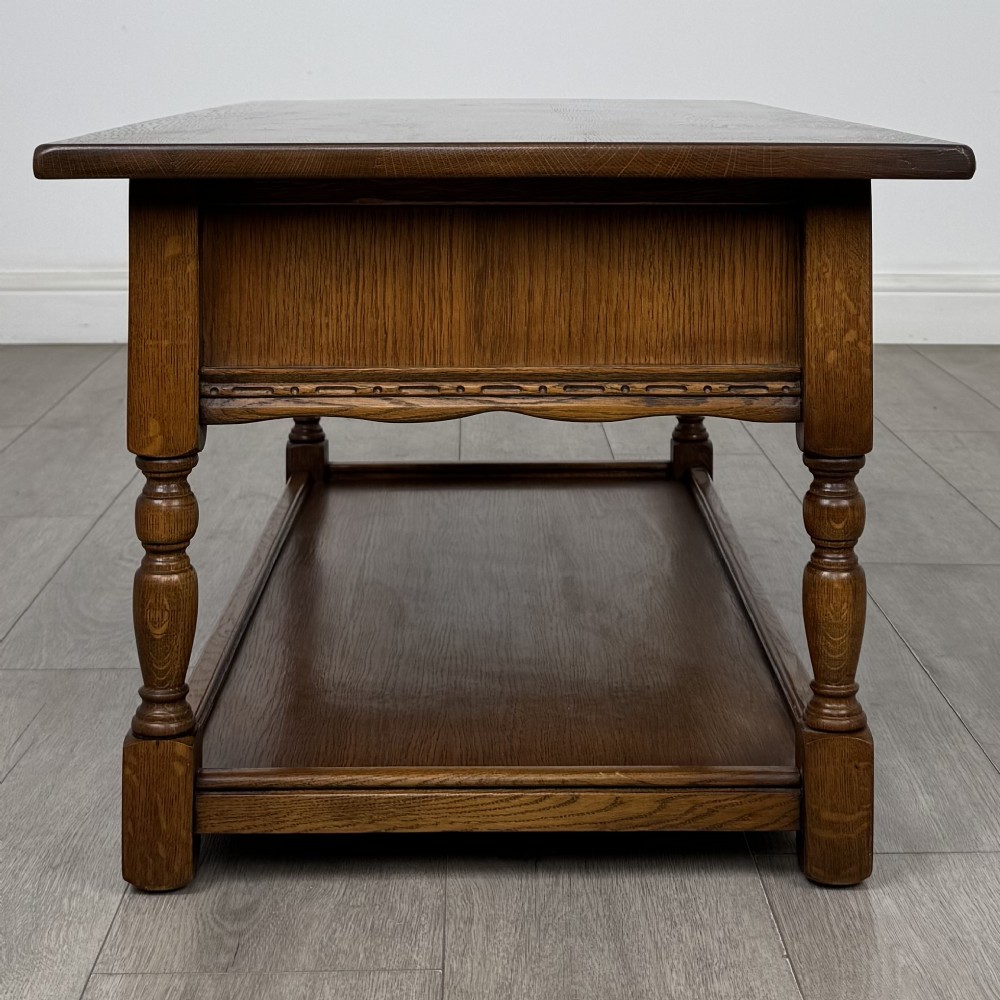 A rectangular warm brown oak coffee table featuring two drawers with metal ring handles, carved apron detailing, turned legs, and a lower storage shelf. View III