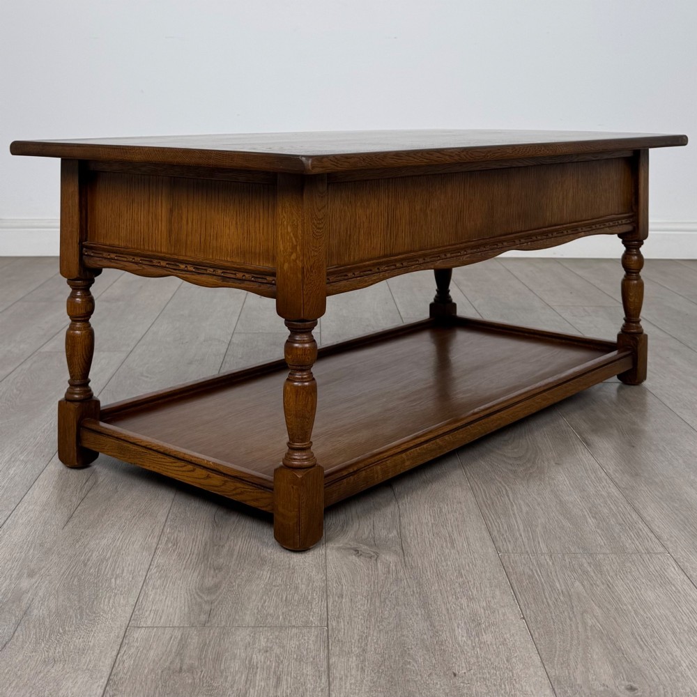 A rectangular warm brown oak coffee table featuring two drawers with metal ring handles, carved apron detailing, turned legs, and a lower storage shelf. View IV