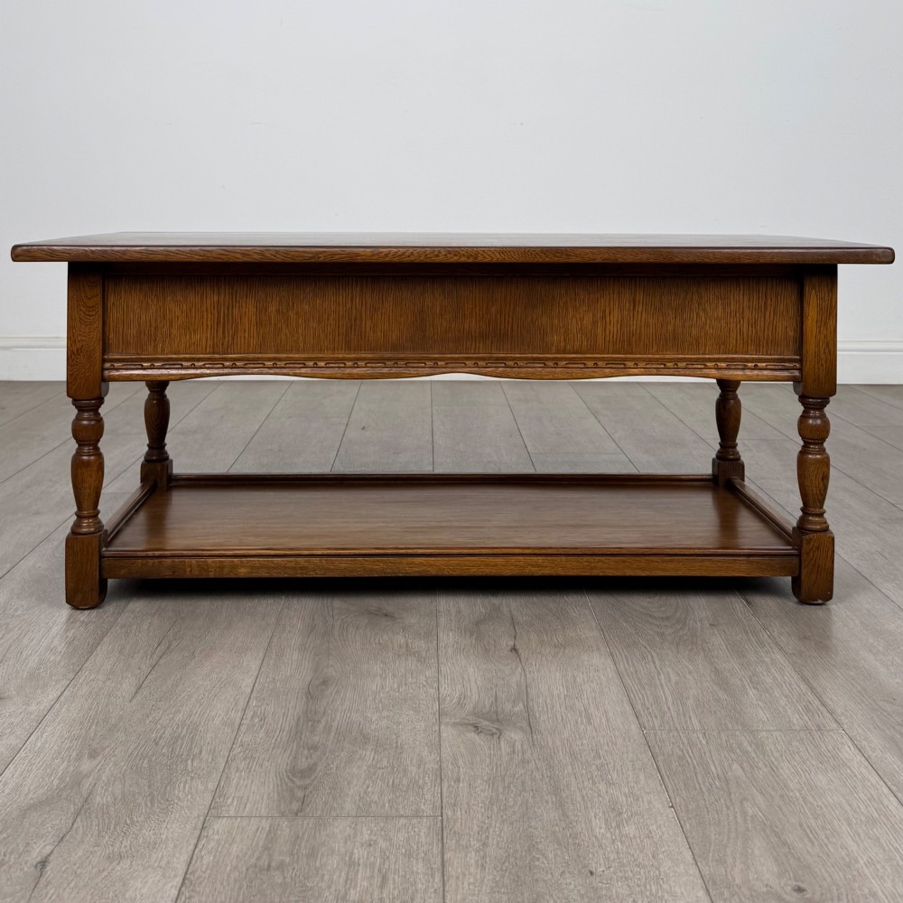 A rectangular warm brown oak coffee table featuring two drawers with metal ring handles, carved apron detailing, turned legs, and a lower storage shelf. View V