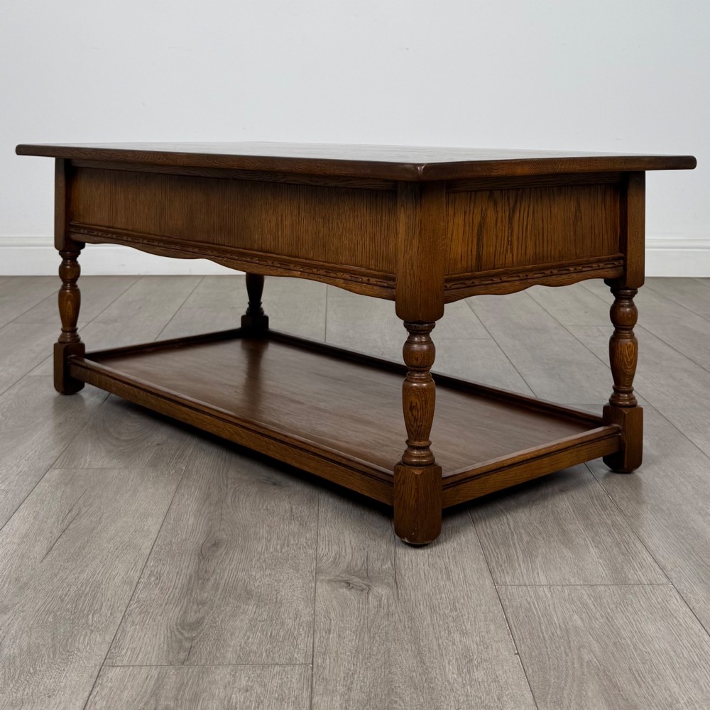 A rectangular warm brown oak coffee table featuring two drawers with metal ring handles, carved apron detailing, turned legs, and a lower storage shelf. View VI