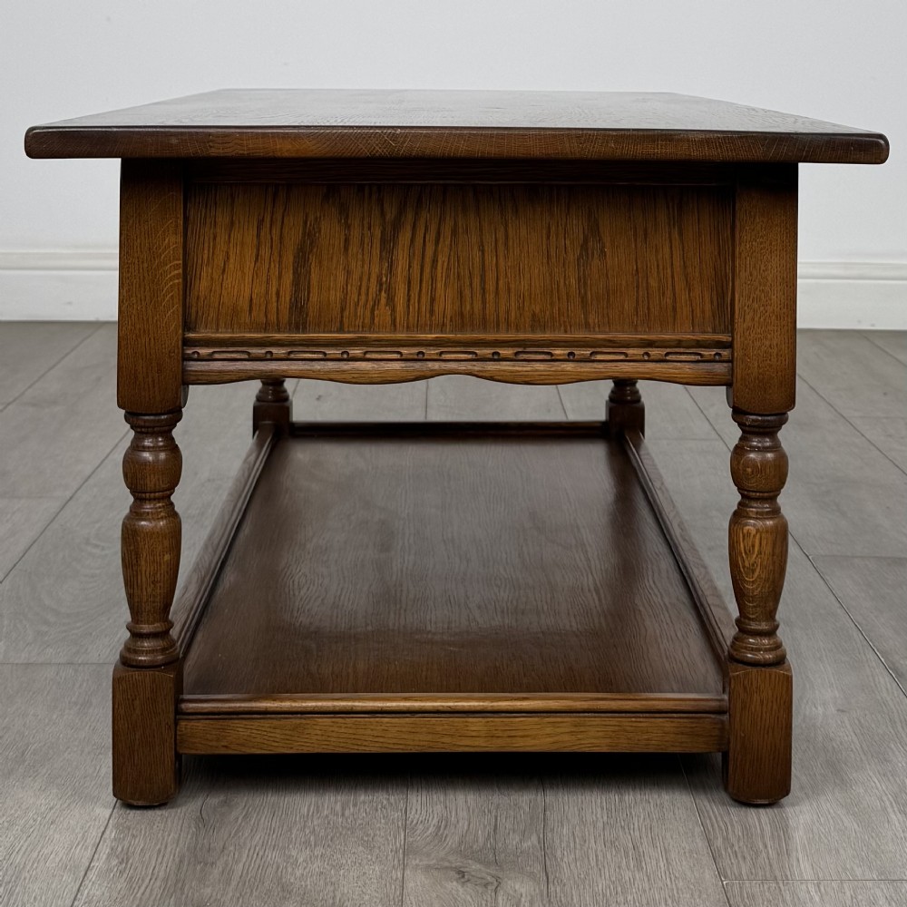 A rectangular warm brown oak coffee table featuring two drawers with metal ring handles, carved apron detailing, turned legs, and a lower storage shelf. View VII