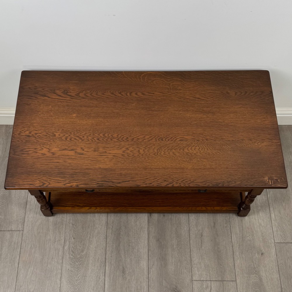A rectangular warm brown oak coffee table featuring two drawers with metal ring handles, carved apron detailing, turned legs, and a lower storage shelf. View IX