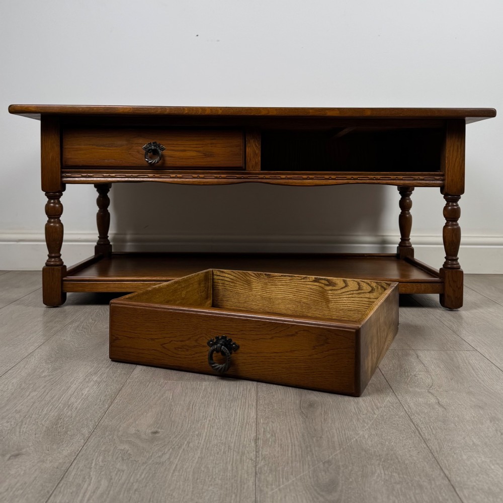 A rectangular warm brown oak coffee table featuring two drawers with metal ring handles, carved apron detailing, turned legs, and a lower storage shelf. View X