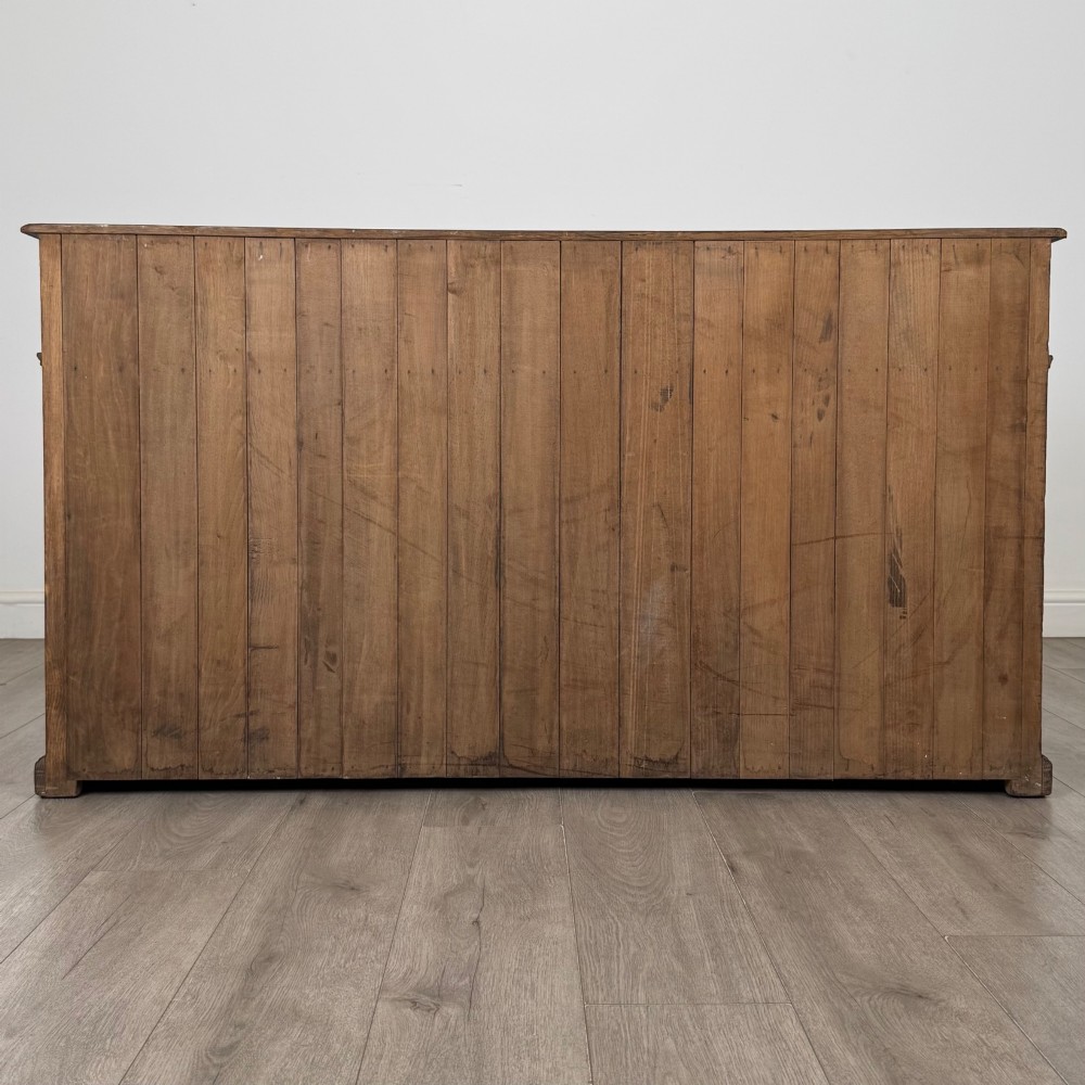 An antique golden oak dresser base featuring three top drawers, two panelled outer doors, and a central arched open recess. View VI