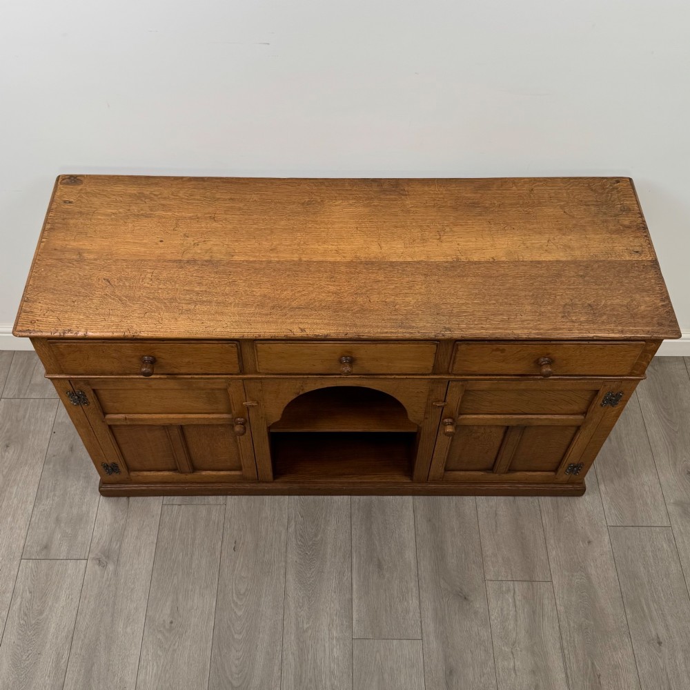 An antique golden oak dresser base featuring three top drawers, two panelled outer doors, and a central arched open recess. View X