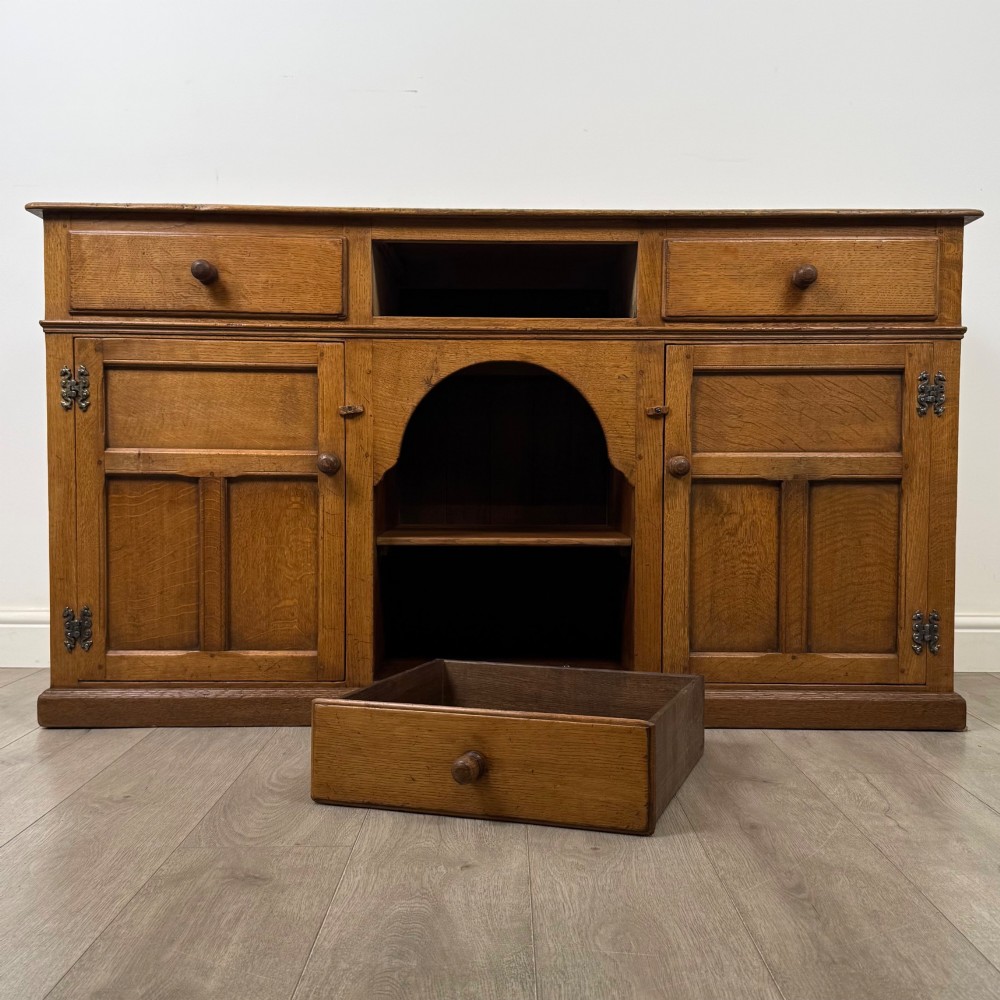 An antique golden oak dresser base featuring three top drawers, two panelled outer doors, and a central arched open recess. View XI
