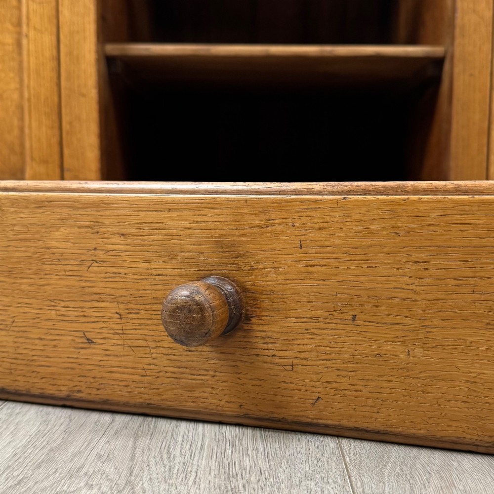 An antique golden oak dresser base featuring three top drawers, two panelled outer doors, and a central arched open recess. View XII