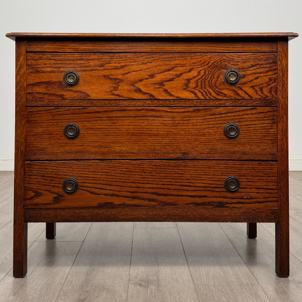 An Edwardian oak chest of drawers featuring three full-width drawers with circular pull handles, supported by straight square legs.