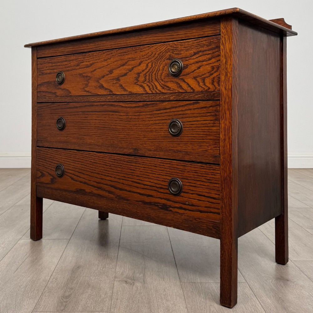 An Edwardian oak chest of drawers featuring three full-width drawers with circular pull handles, supported by straight square legs. View II