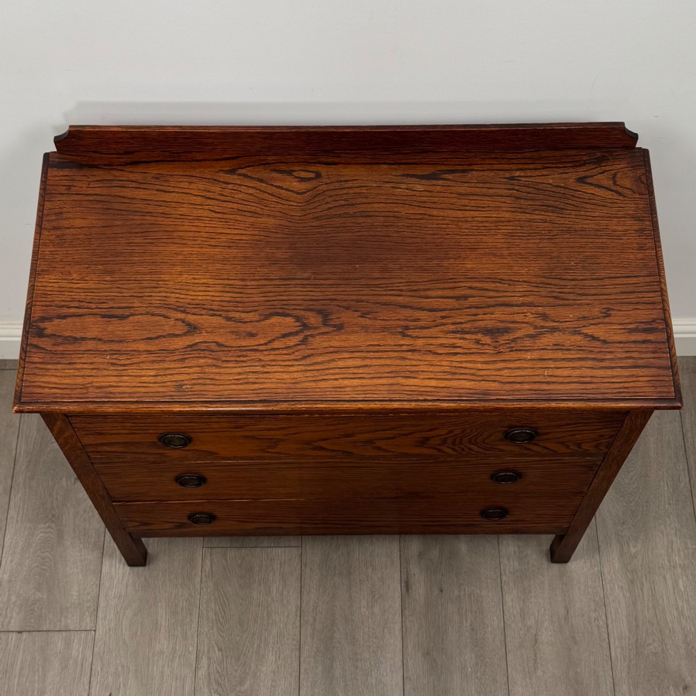 An Edwardian oak chest of drawers featuring three full-width drawers with circular pull handles, supported by straight square legs. View IX