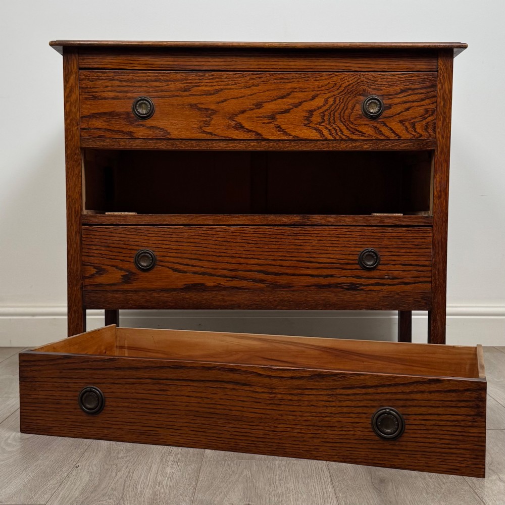 An Edwardian oak chest of drawers featuring three full-width drawers with circular pull handles, supported by straight square legs. View X