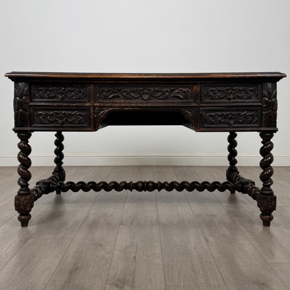 A 19th-century dark oak writing table featuring carved drawer fronts, barley twist legs, and a low spiral stretcher.
