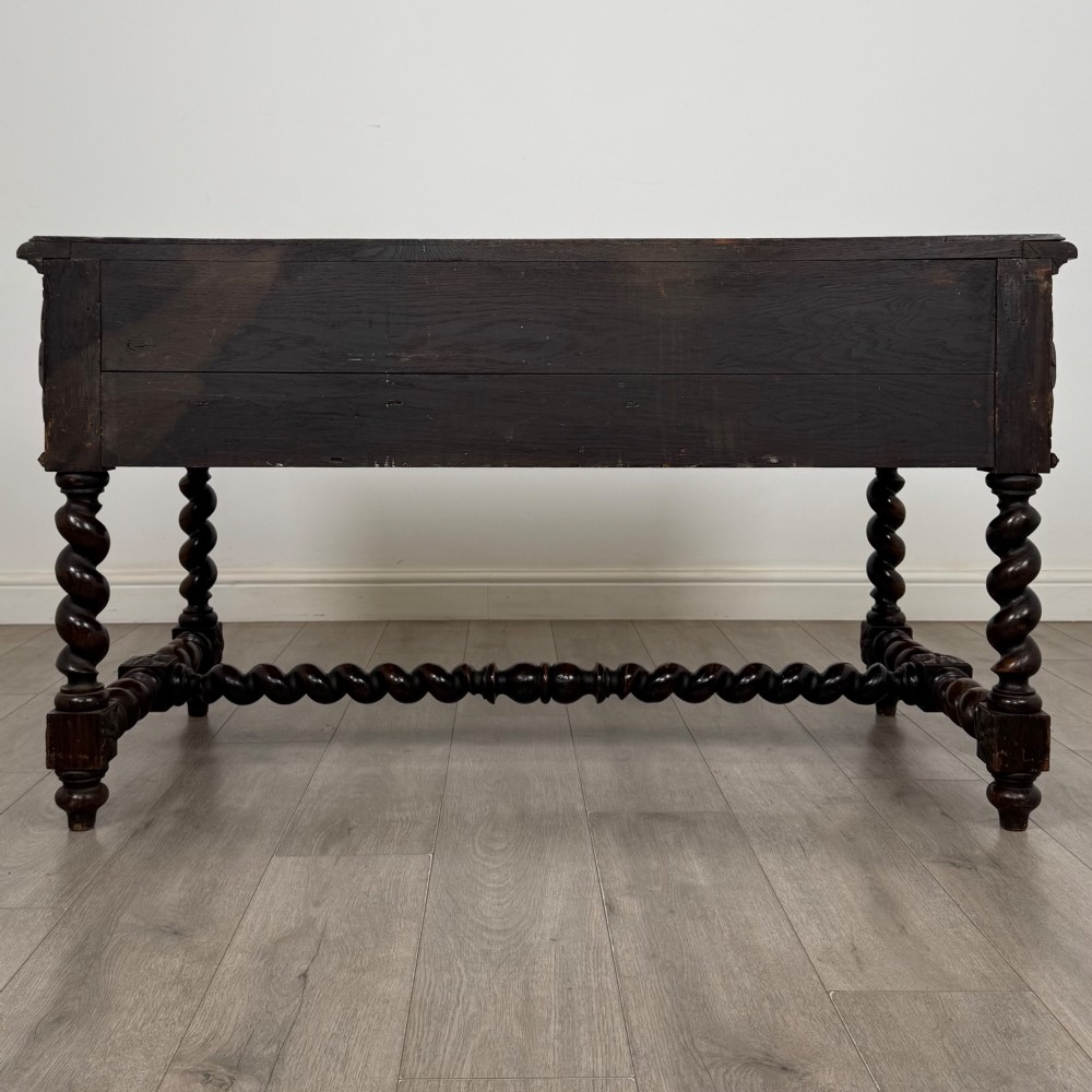 A 19th-century dark oak writing table featuring carved drawer fronts, barley twist legs, and a low spiral stretcher. View V
