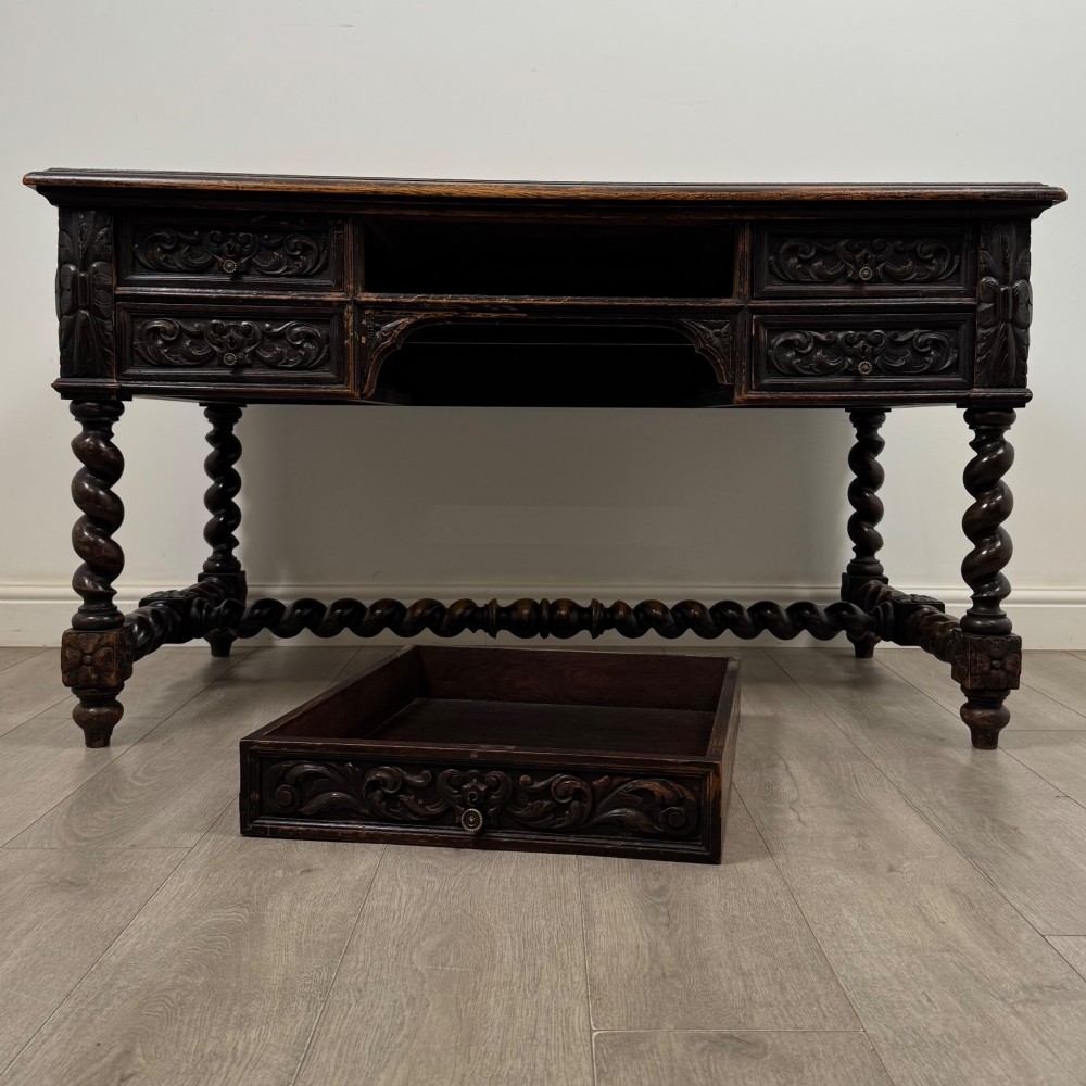 A 19th-century dark oak writing table featuring carved drawer fronts, barley twist legs, and a low spiral stretcher. View X