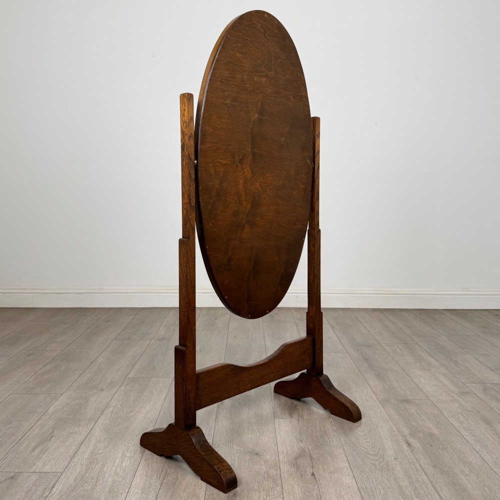 An Edwardian oak cheval mirror featuring an oval glass frame suspended between two upright posts on trestle feet. View III