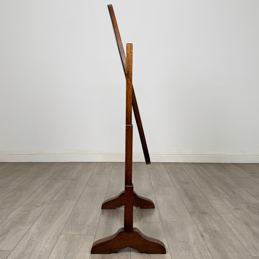 An Edwardian oak cheval mirror featuring an oval glass frame suspended between two upright posts on trestle feet. View VI