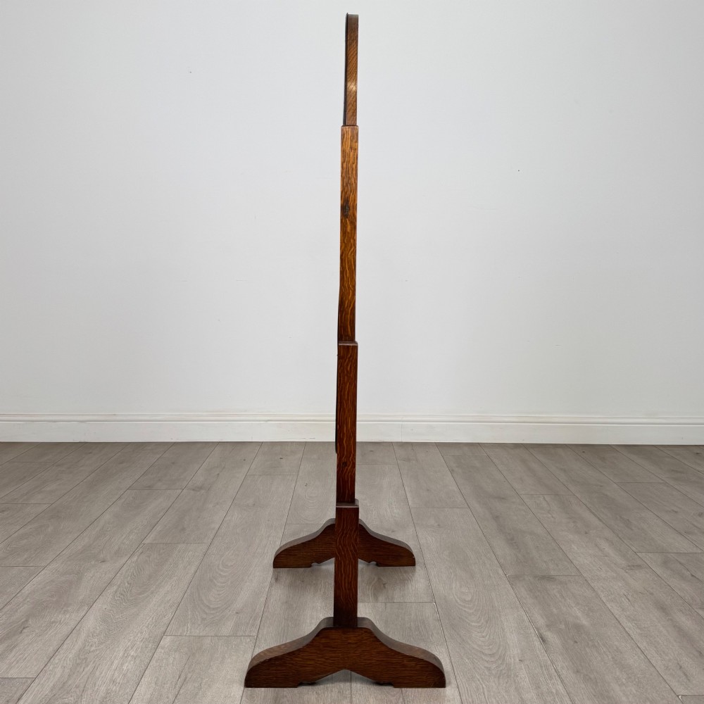 An Edwardian oak cheval mirror featuring an oval glass frame suspended between two upright posts on trestle feet. View VII