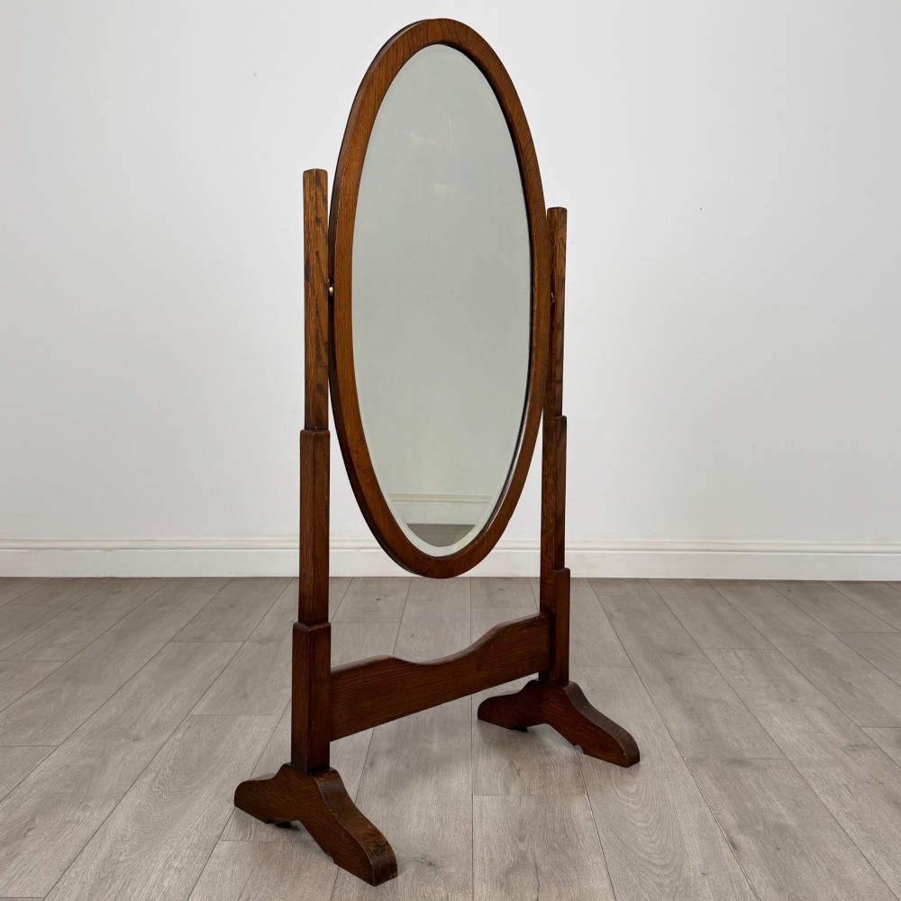 An Edwardian oak cheval mirror featuring an oval glass frame suspended between two upright posts on trestle feet. View VIII
