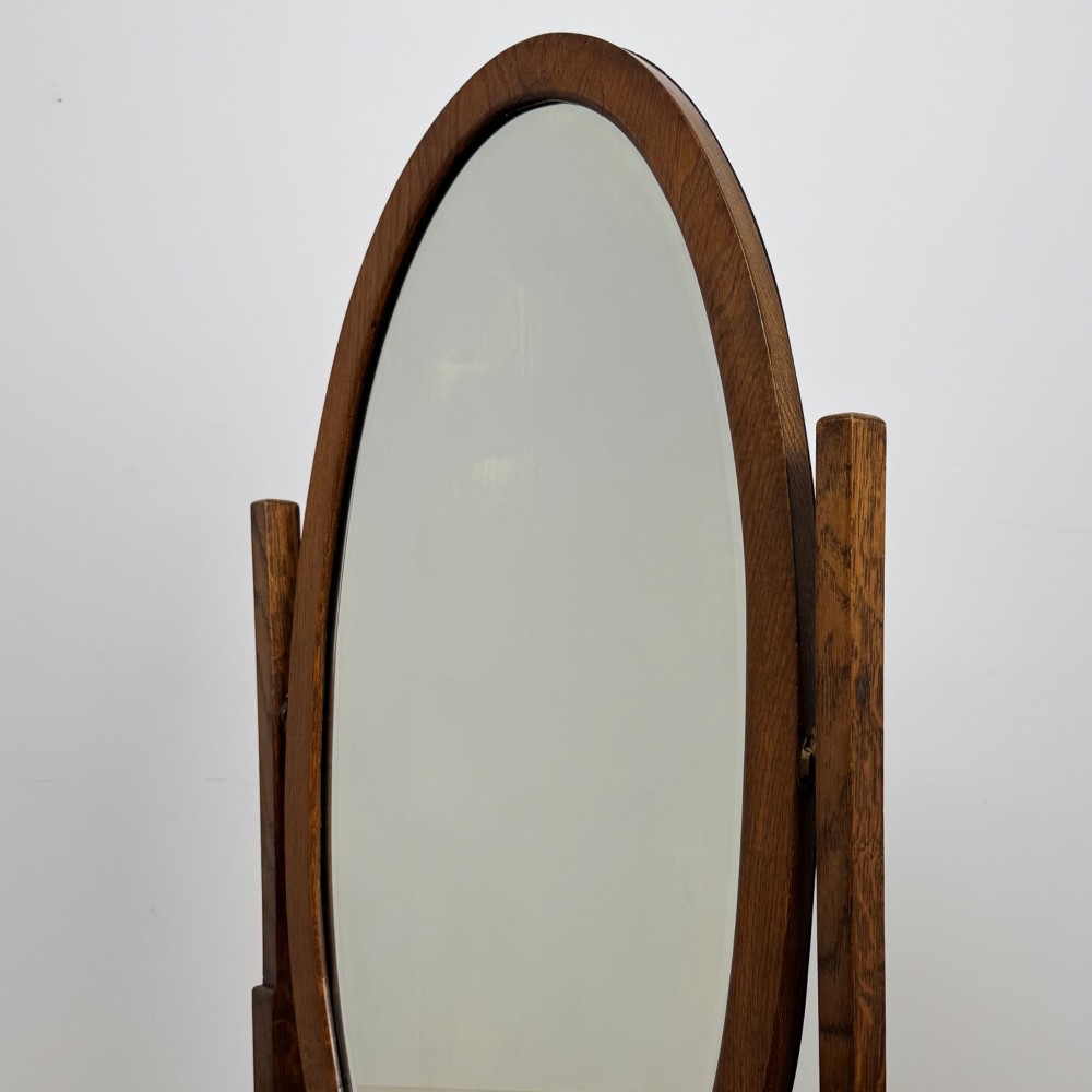 An Edwardian oak cheval mirror featuring an oval glass frame suspended between two upright posts on trestle feet. View XII