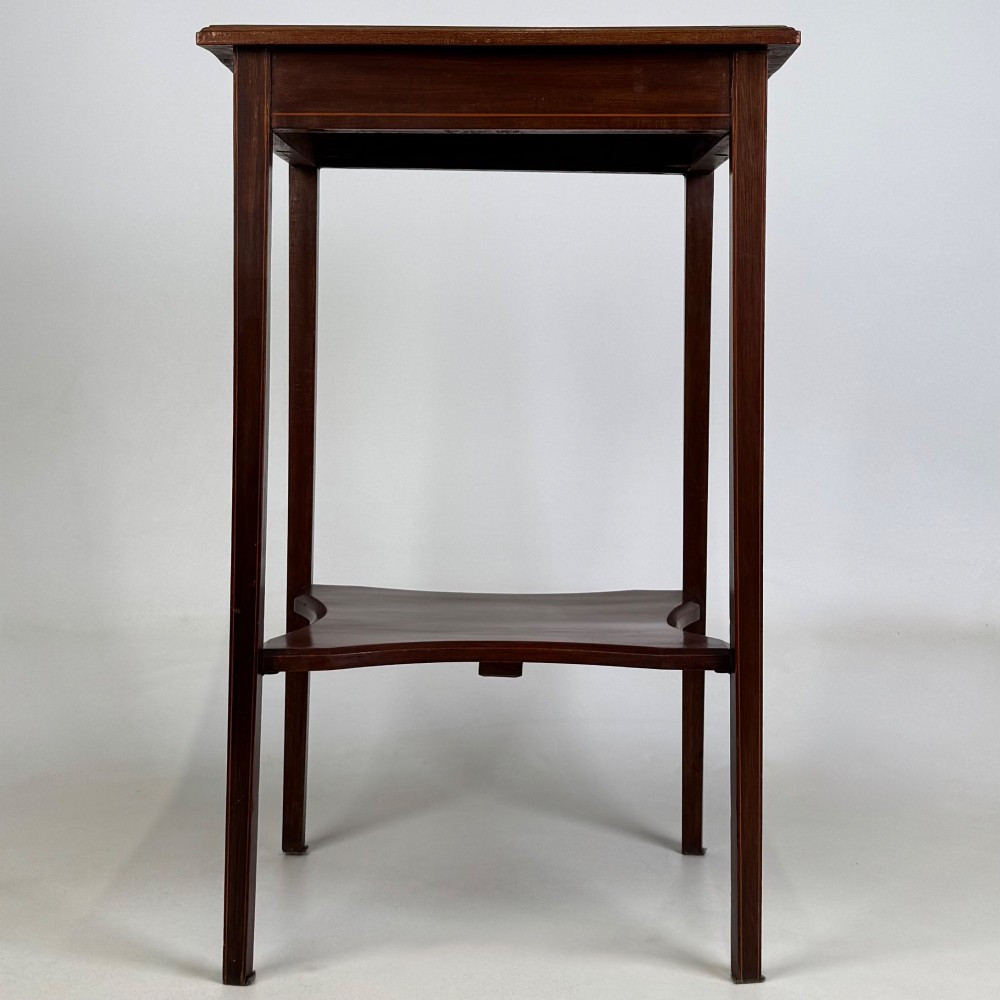 A tall Edwardian mahogany side table featuring four slender tapered legs, a square top surface, and a concave-shaped lower undertier.