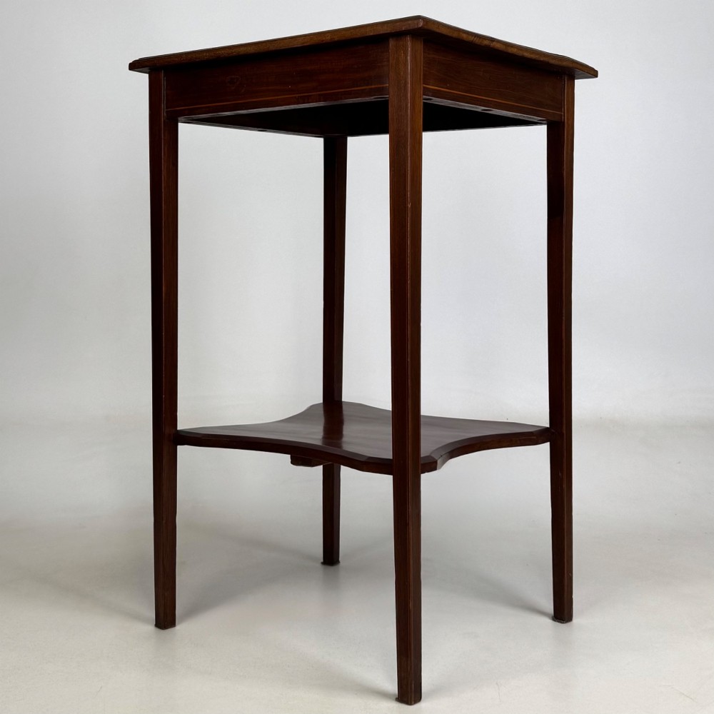 A tall Edwardian mahogany side table featuring four slender tapered legs, a square top surface, and a concave-shaped lower undertier. View VI