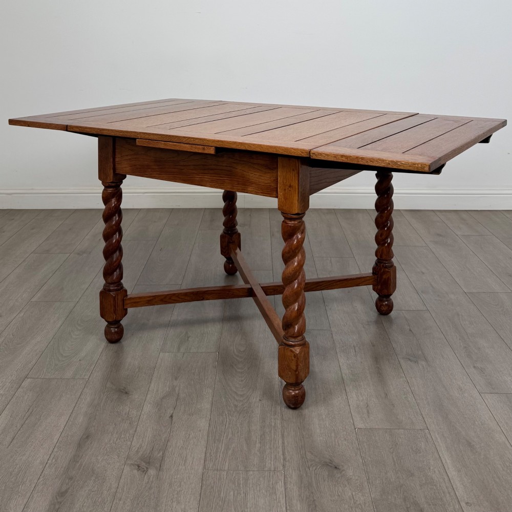 An Edwardian warm oak draw leaf dining table featuring extended side leaves, barley twist legs, and an X-frame cross stretcher.