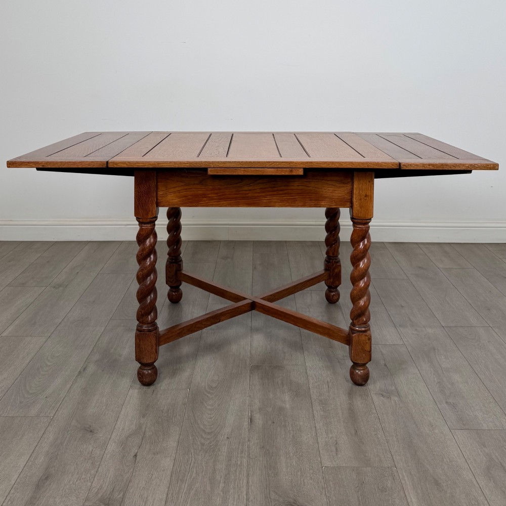 An Edwardian warm oak draw leaf dining table featuring extended side leaves, barley twist legs, and an X-frame cross stretcher. View II
