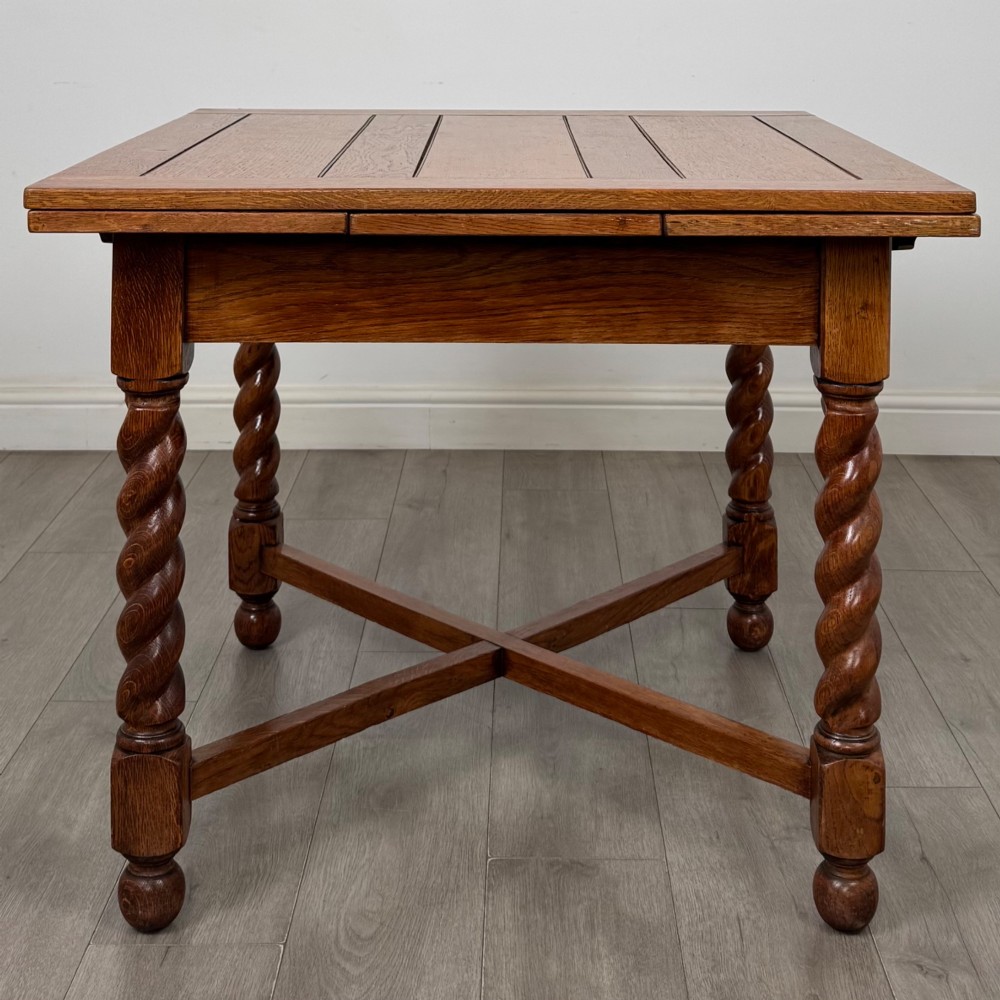 An Edwardian warm oak draw leaf dining table featuring extended side leaves, barley twist legs, and an X-frame cross stretcher. View III