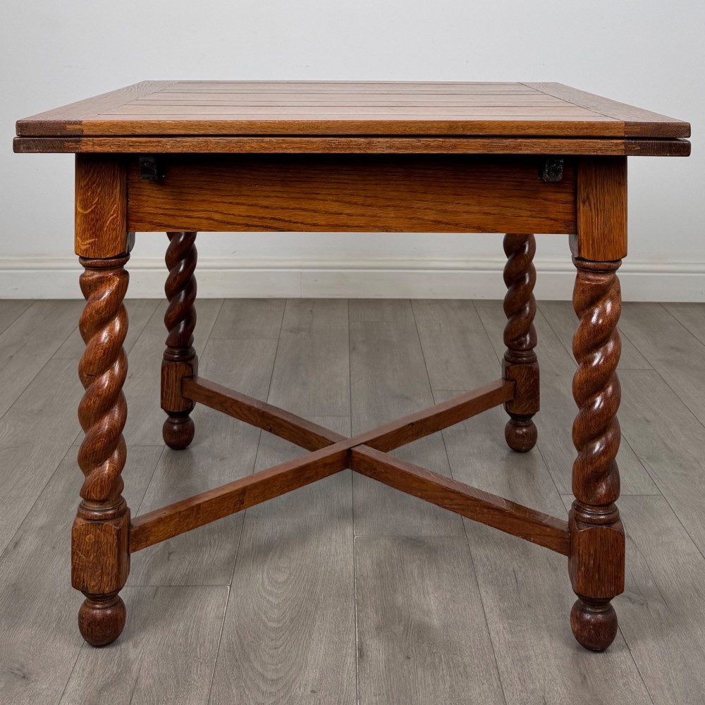 An Edwardian warm oak draw leaf dining table featuring extended side leaves, barley twist legs, and an X-frame cross stretcher. View IV