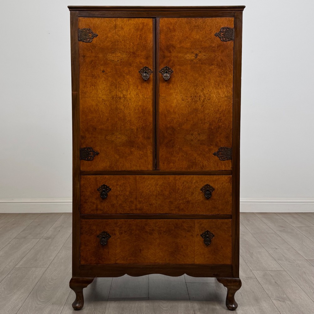 An Edwardian burr walnut storage cupboard featuring two top doors with brass strap hinges above two drawers on cabriole legs.
