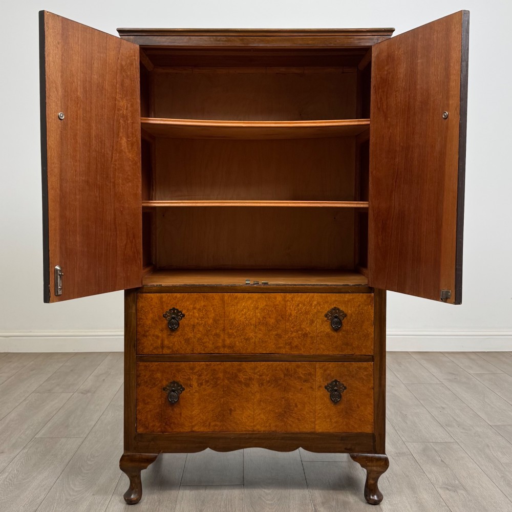 An Edwardian burr walnut storage cupboard featuring two top doors with brass strap hinges above two drawers on cabriole legs. View II