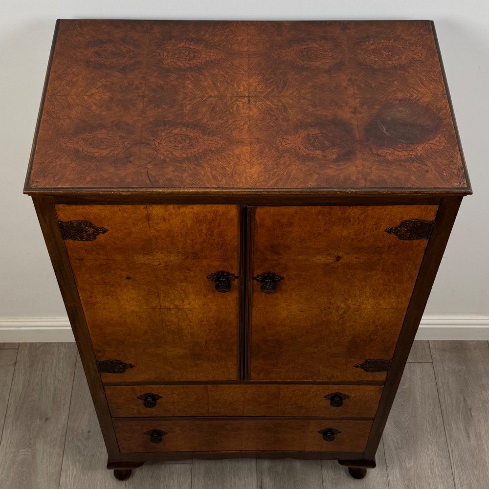 An Edwardian burr walnut storage cupboard featuring two top doors with brass strap hinges above two drawers on cabriole legs. View X