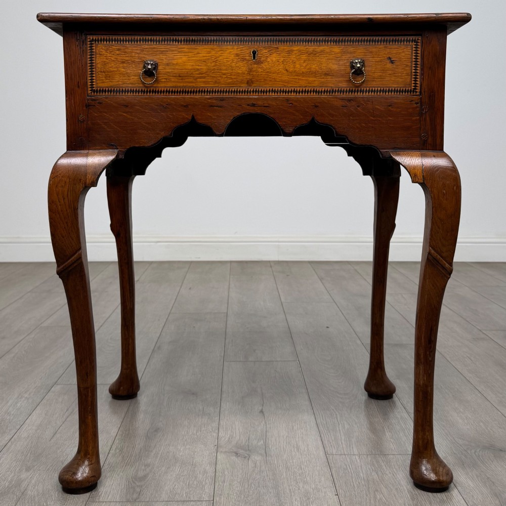 An 18th-century Georgian oak side table featuring a single drawer with geometric inlaid border, lion mask brass ring handles, shaped apron, and four cabriole legs ending in pad feet.