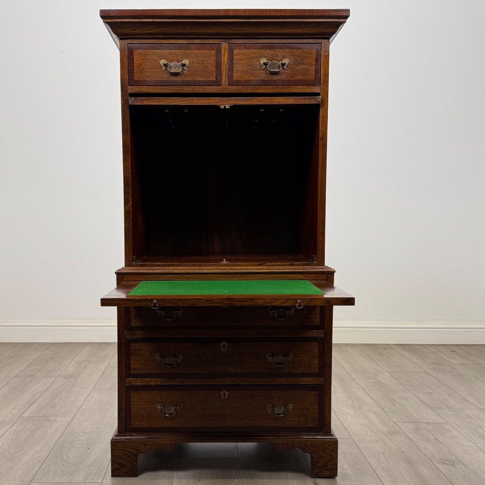 A tall early 20th-century oak chest on chest featuring multiple drawers with crossbanded borders and brass drop handles set on bracket feet. View II