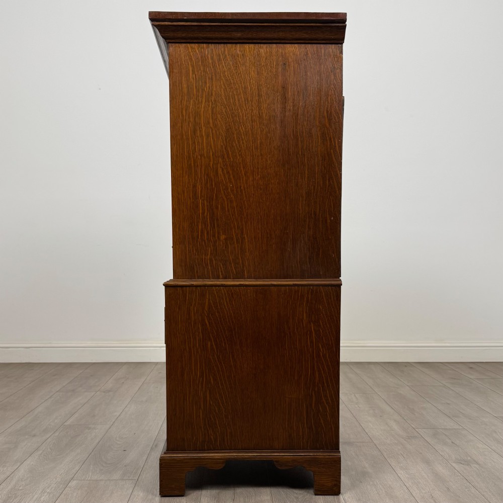 A tall early 20th-century oak chest on chest featuring multiple drawers with crossbanded borders and brass drop handles set on bracket feet. View IV