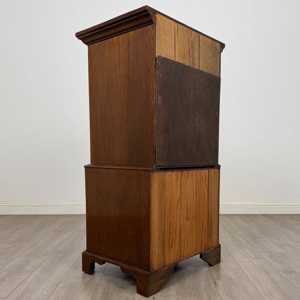 A tall early 20th-century oak chest on chest featuring multiple drawers with crossbanded borders and brass drop handles set on bracket feet. View V