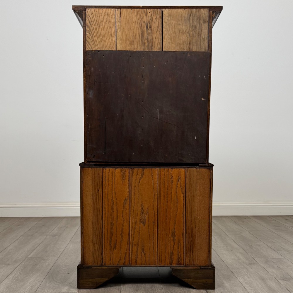 A tall early 20th-century oak chest on chest featuring multiple drawers with crossbanded borders and brass drop handles set on bracket feet. View VI