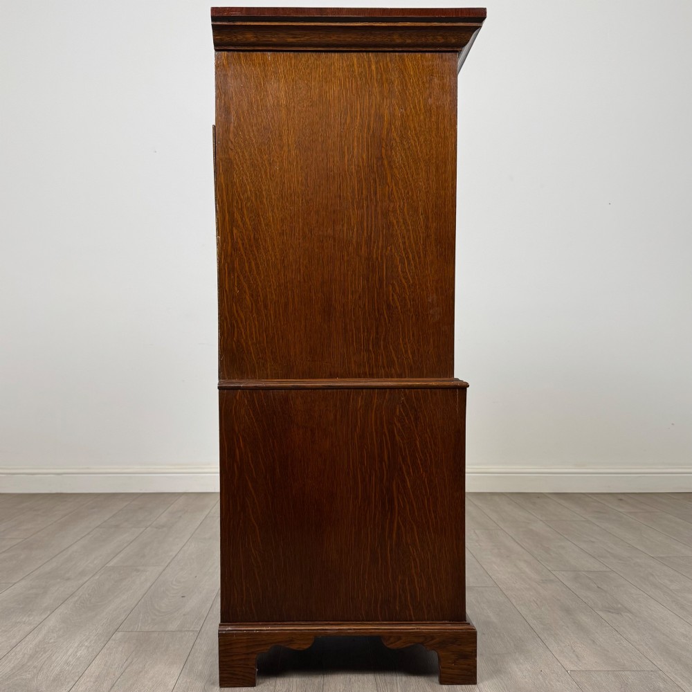A tall early 20th-century oak chest on chest featuring multiple drawers with crossbanded borders and brass drop handles set on bracket feet. View VIII