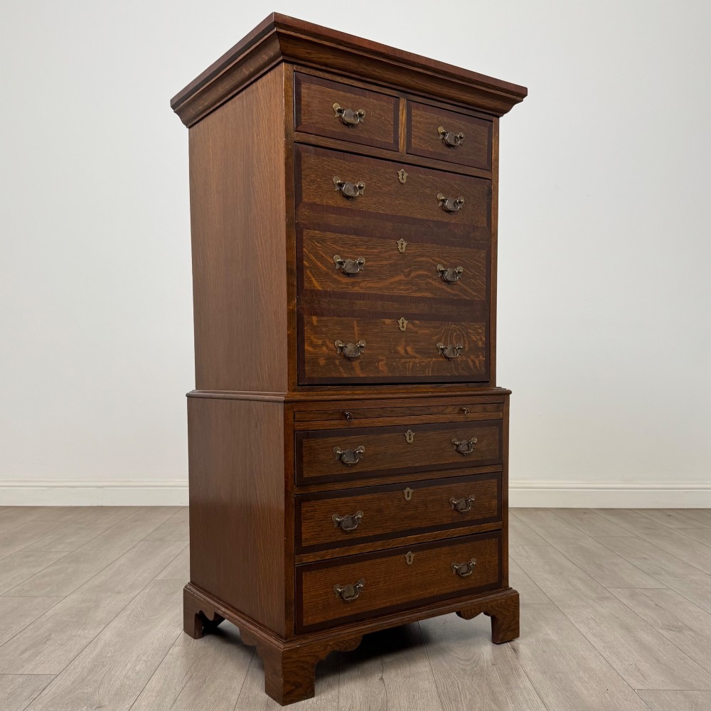 A tall early 20th-century oak chest on chest featuring multiple drawers with crossbanded borders and brass drop handles set on bracket feet. View IX
