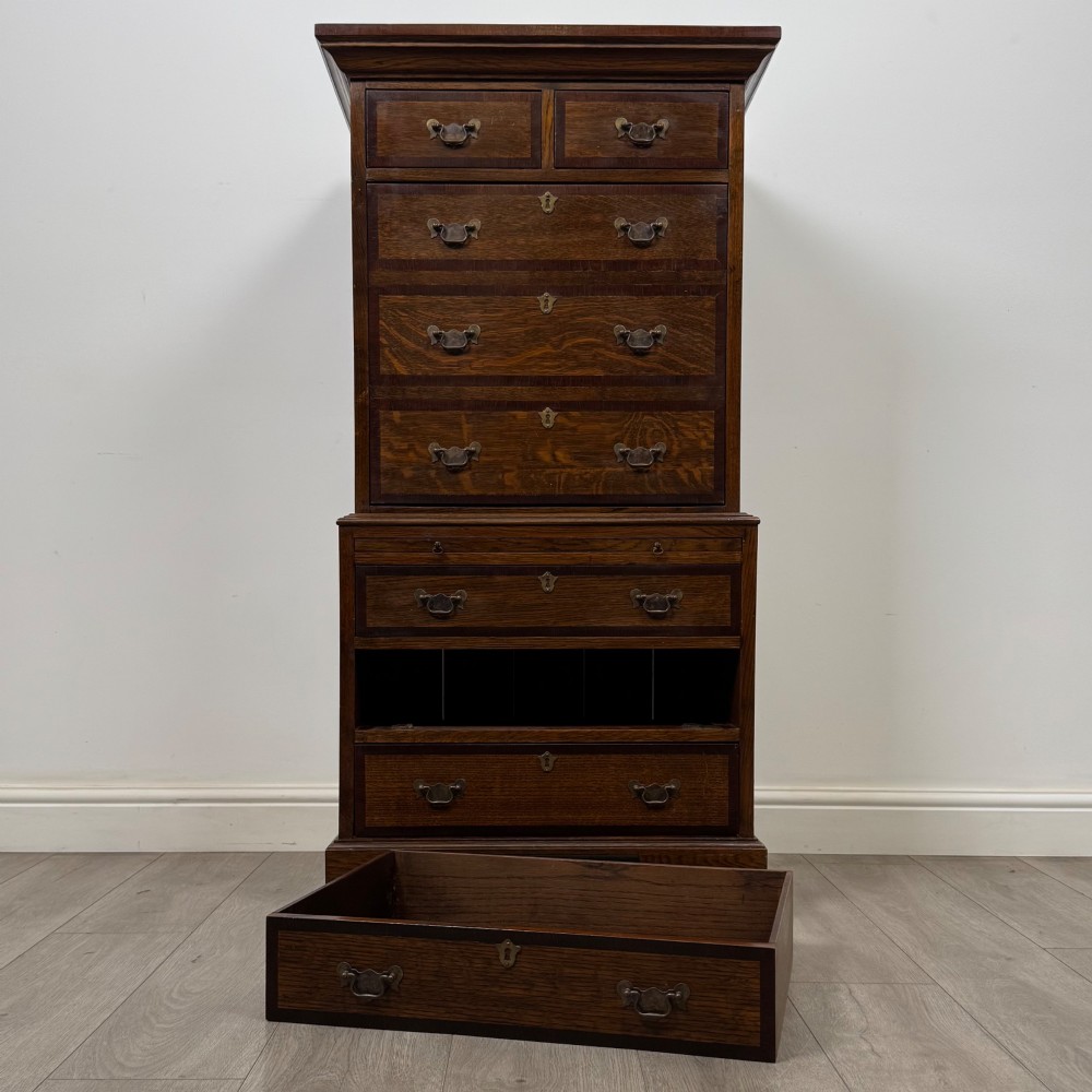 A tall early 20th-century oak chest on chest featuring multiple drawers with crossbanded borders and brass drop handles set on bracket feet. View XII