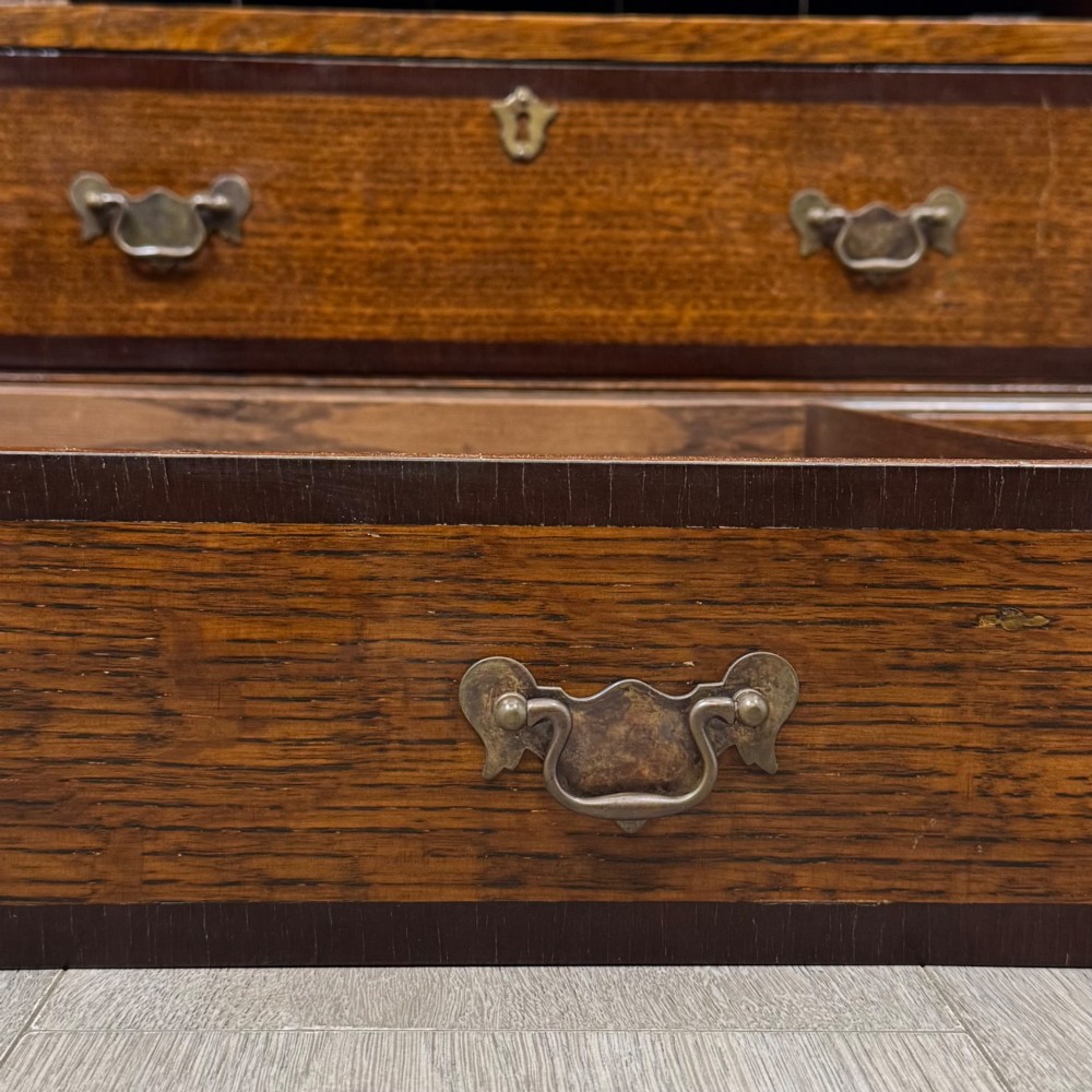A tall early 20th-century oak chest on chest featuring multiple drawers with crossbanded borders and brass drop handles set on bracket feet. View XIII