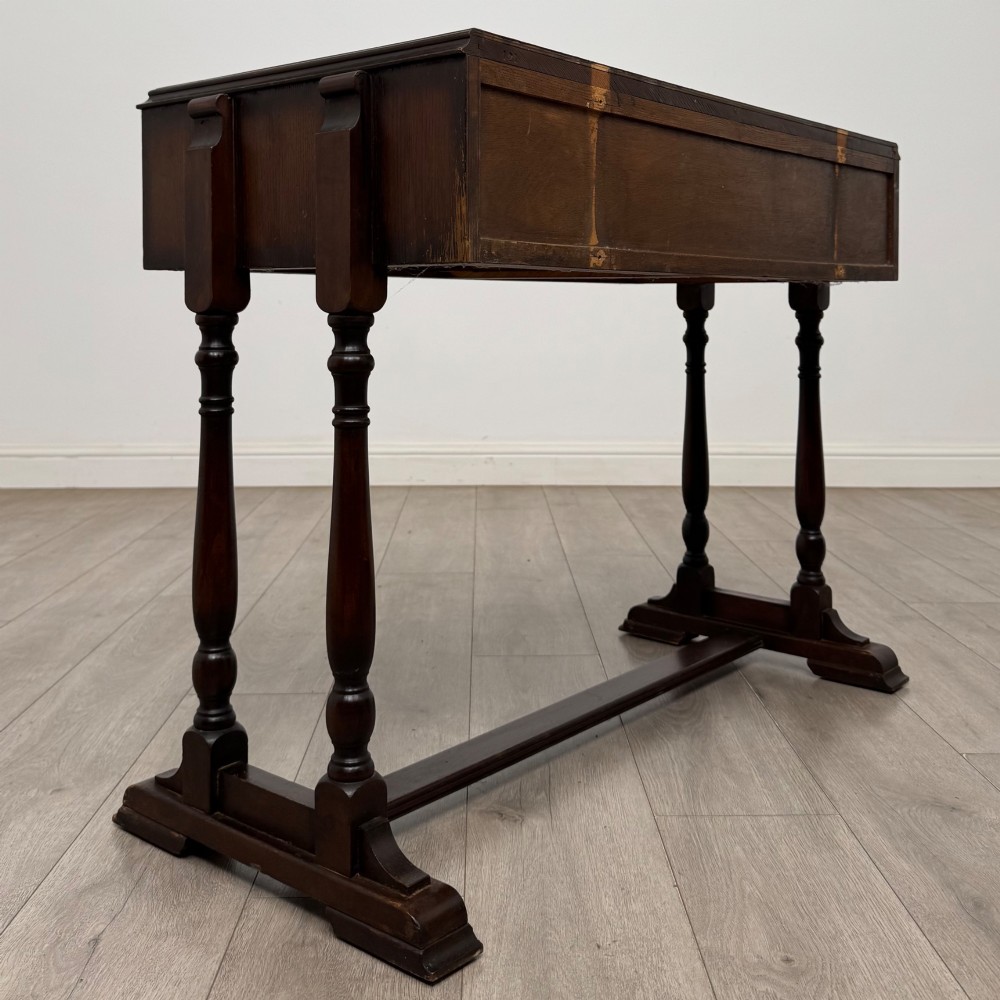 A dark brown carved oak side table featuring two scroll-carved front drawers with metal drop handles and turned trestle legs. View IV