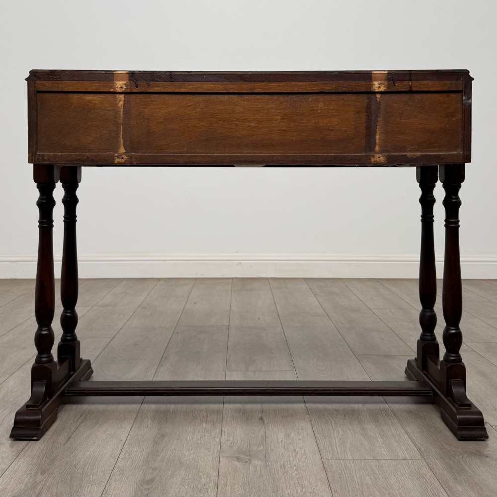 A dark brown carved oak side table featuring two scroll-carved front drawers with metal drop handles and turned trestle legs. View V