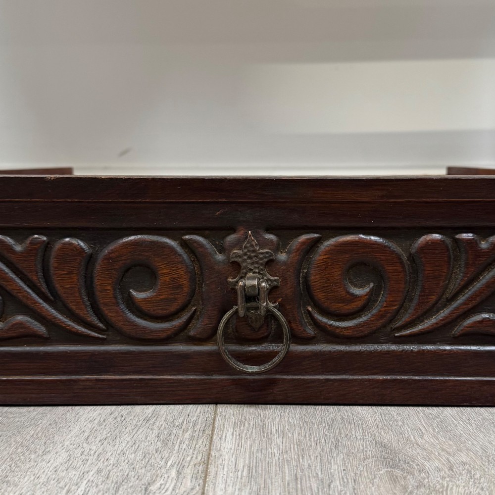 A dark brown carved oak side table featuring two scroll-carved front drawers with metal drop handles and turned trestle legs. View XI